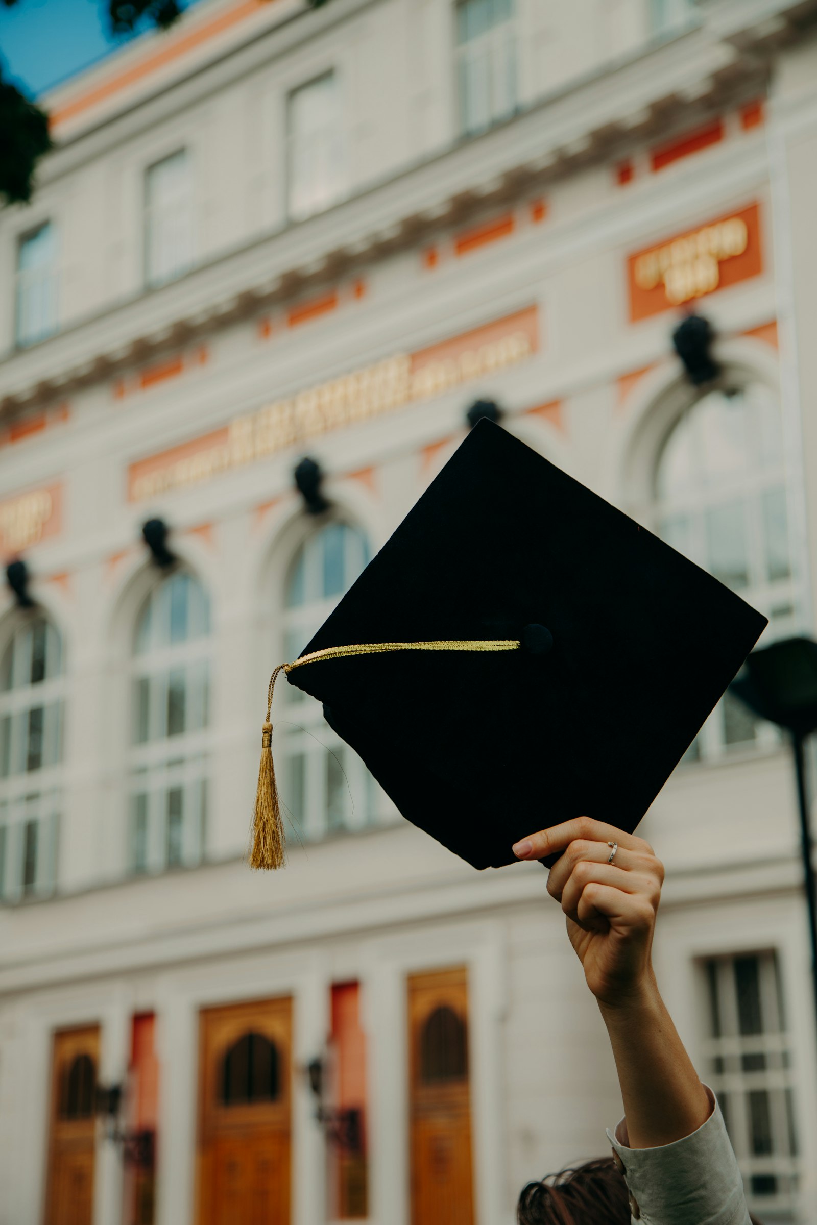 Graduado levantando su birrete frente a la universidad